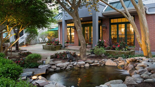 A landscaped garden with a pond, stone pathway, and a building with large windows and a brick facade. - The Bellmoor Inn & Spa (Rehoboth Beach)