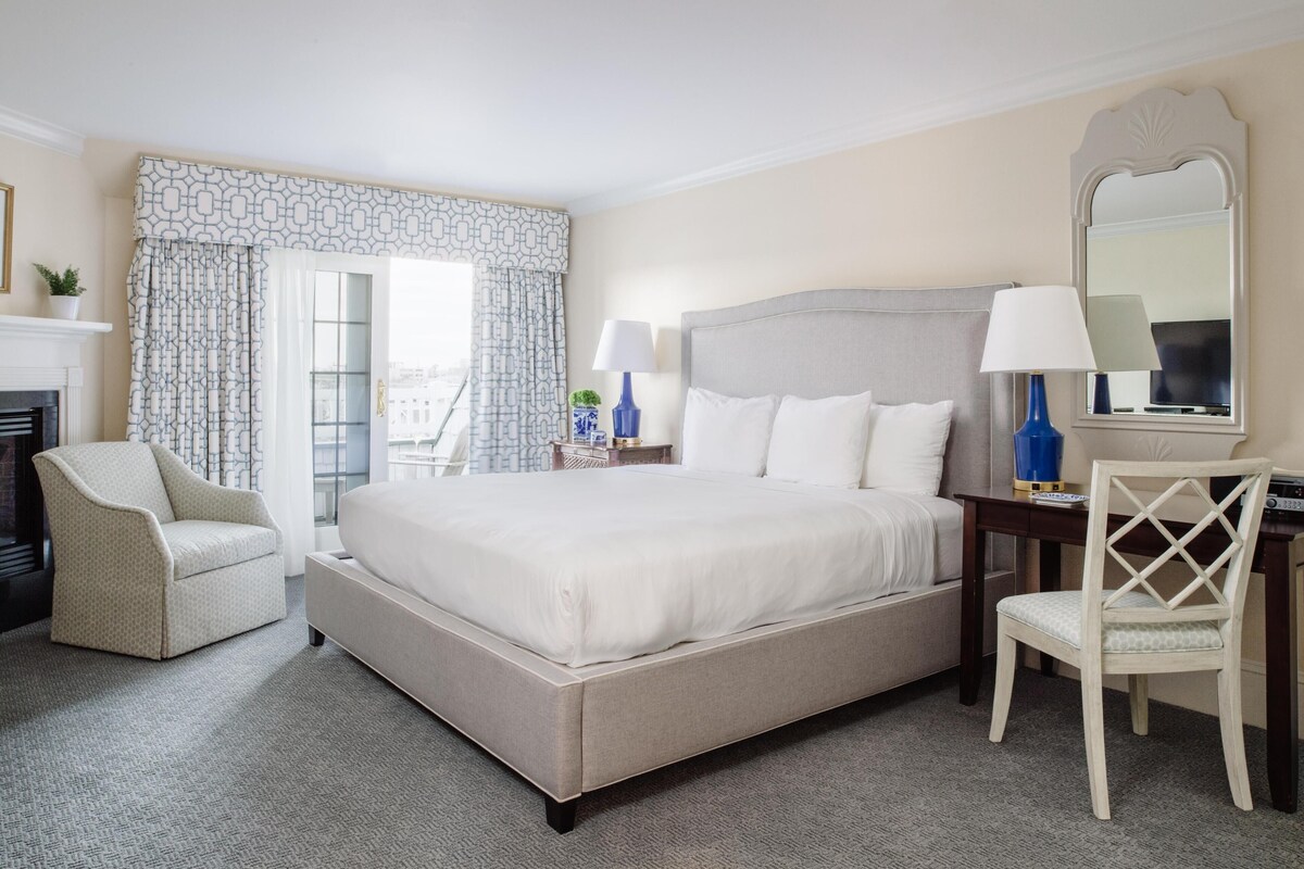 A hotel room with a large bed, a chair, a desk, and a fireplace.