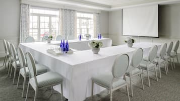 A conference room with a long table, white chairs, and a projector screen.
