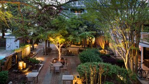 An outdoor patio area with brick flooring, wooden tables and chairs, and trees. - The Bellmoor Inn & Spa (Rehoboth Beach)