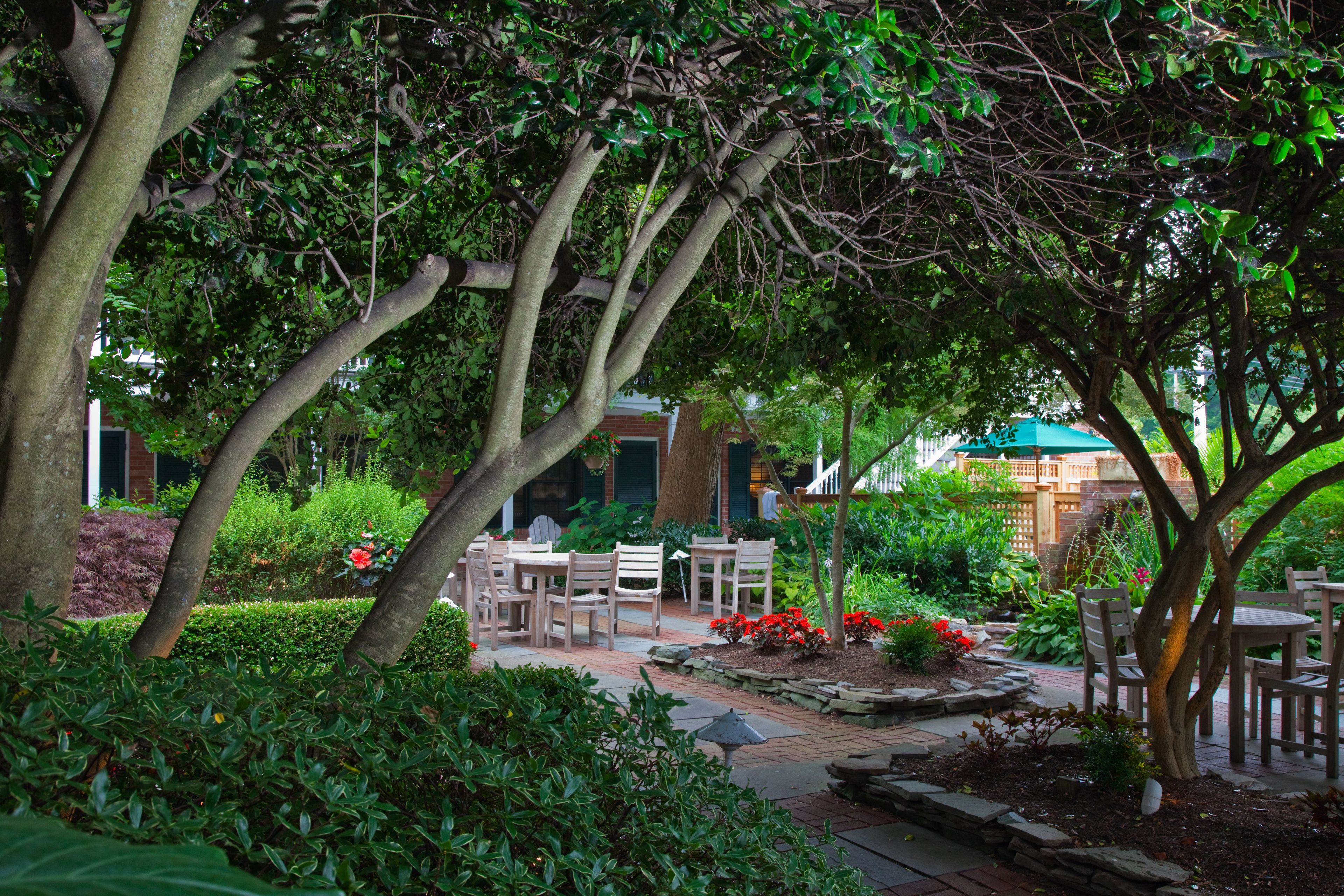 Eine Gartenpatio mit Holzmöbeln, umgeben von üppigem Grün und blühenden Pflanzen.