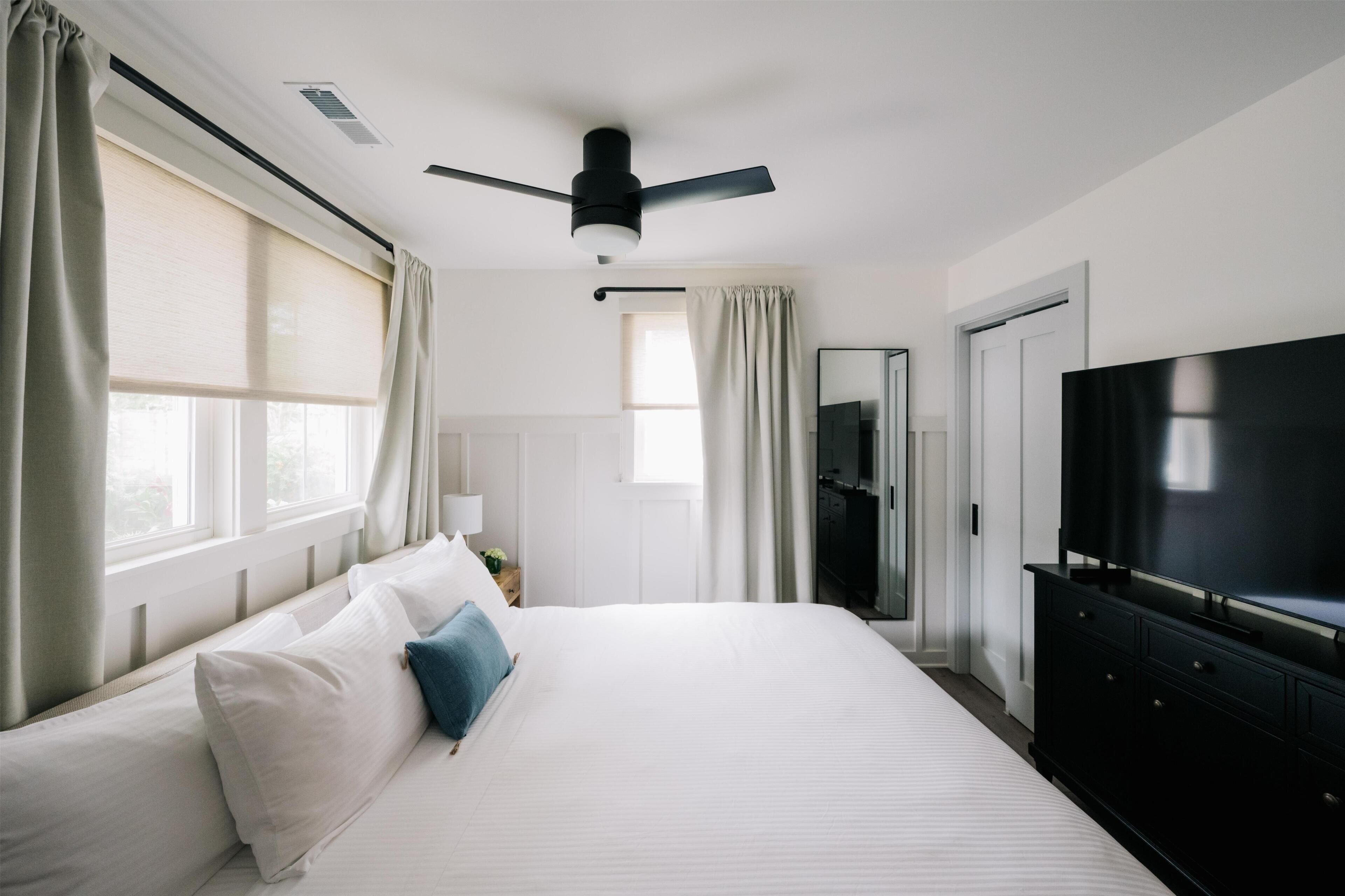 A hotel room with a large bed, a ceiling fan, a TV, and a wardrobe.