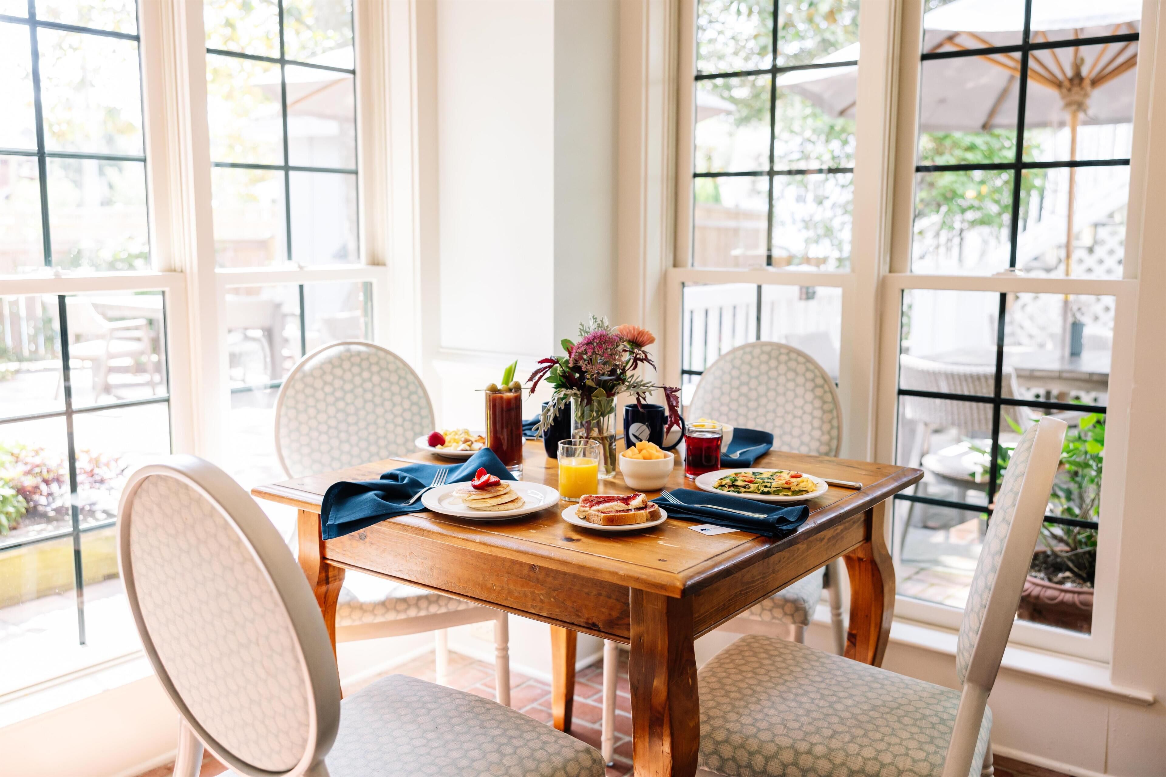 Une table à manger avec des aliments pour le petit-déjeuner, des chaises et de grandes fenêtres.