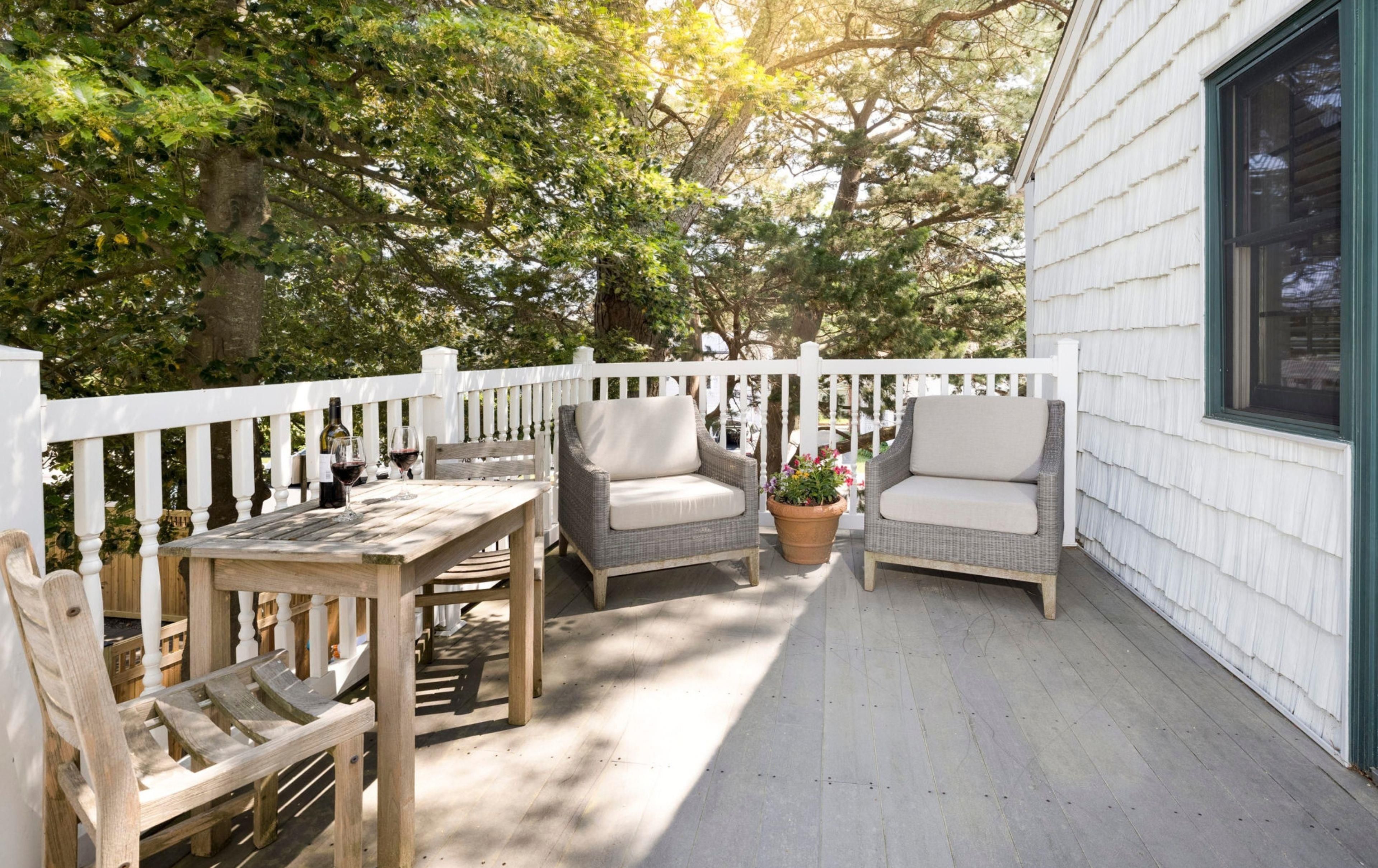 A covered porch with two wicker chairs, a wooden table, and a potted plant.