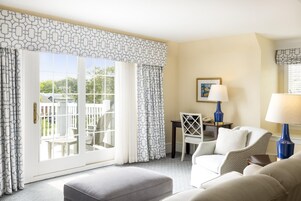 A hotel room with a large sliding glass door leading to a balcony, a desk with a chair, a sofa, and two lamps.