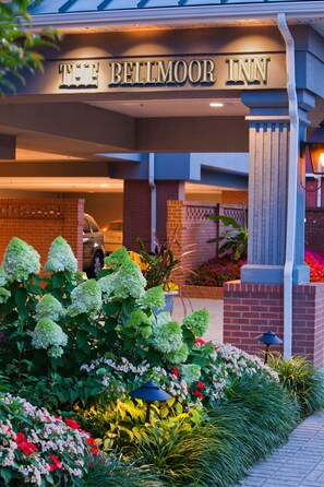 The Bellmoor Inn entrance with a brick facade, a car parked in the background, and a well-maintained garden with various plants and flowers.