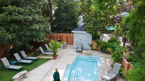 A backyard with a swimming pool, lounge chairs, a small shed, and a wooden fence.