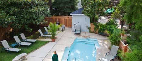 A backyard with a swimming pool, lounge chairs, a small shed, and a wooden fence.
