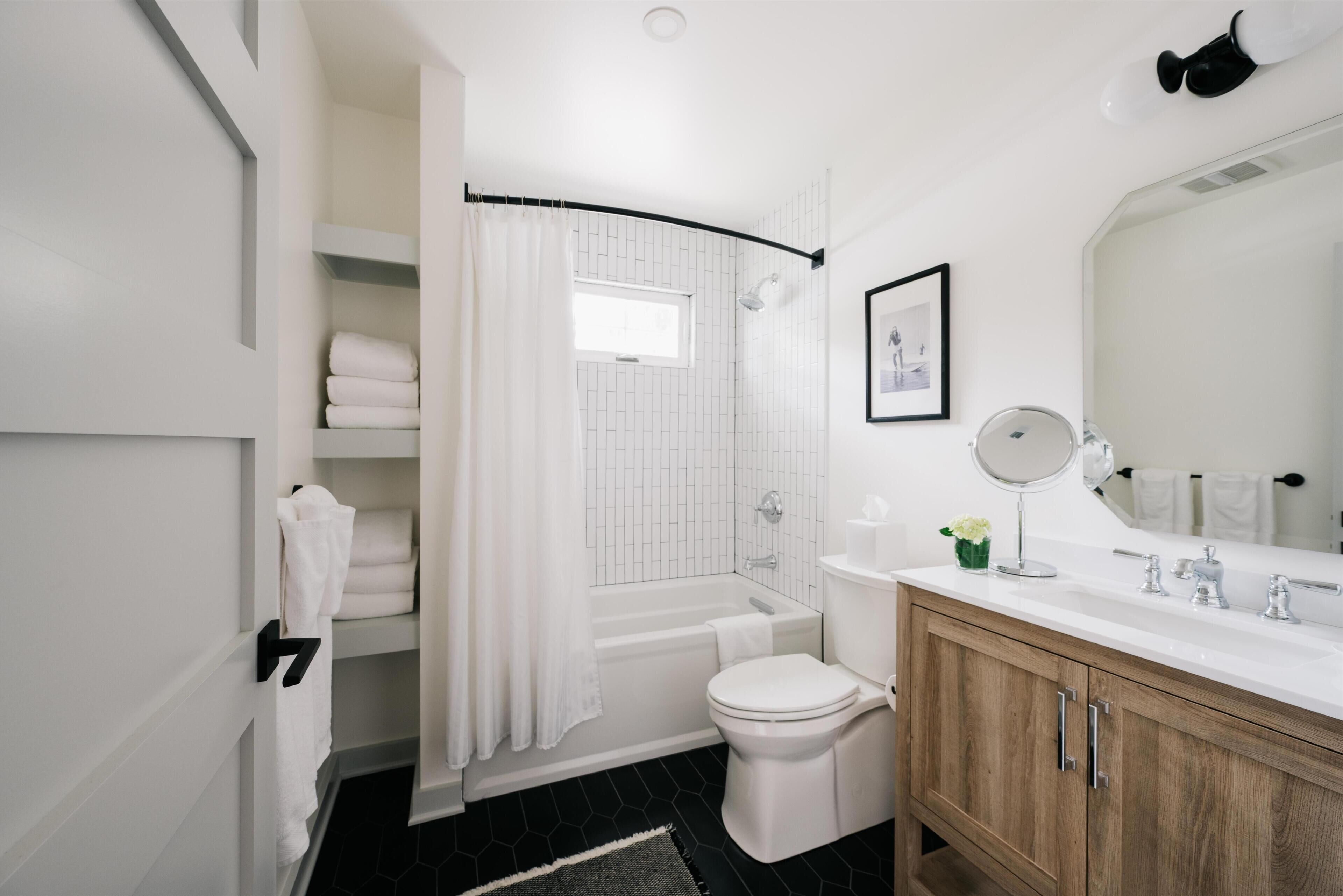 A modern bathroom with a white bathtub, a toilet, a vanity with a mirror, and a shower area.