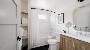 Un bany modern amb una banyera blanca, un vàter, un lavabo amb mirall i una zona de dutxa.