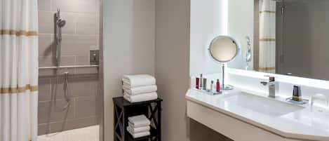 Un baño con ducha, lavabo con espejo y repisas con toallas.