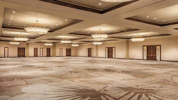A large, empty conference room with a patterned floor, multiple chandeliers, and doors along the walls.
