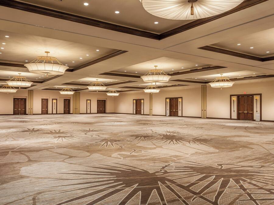 A large, empty conference room with a patterned floor, multiple chandeliers, and doors along the walls.