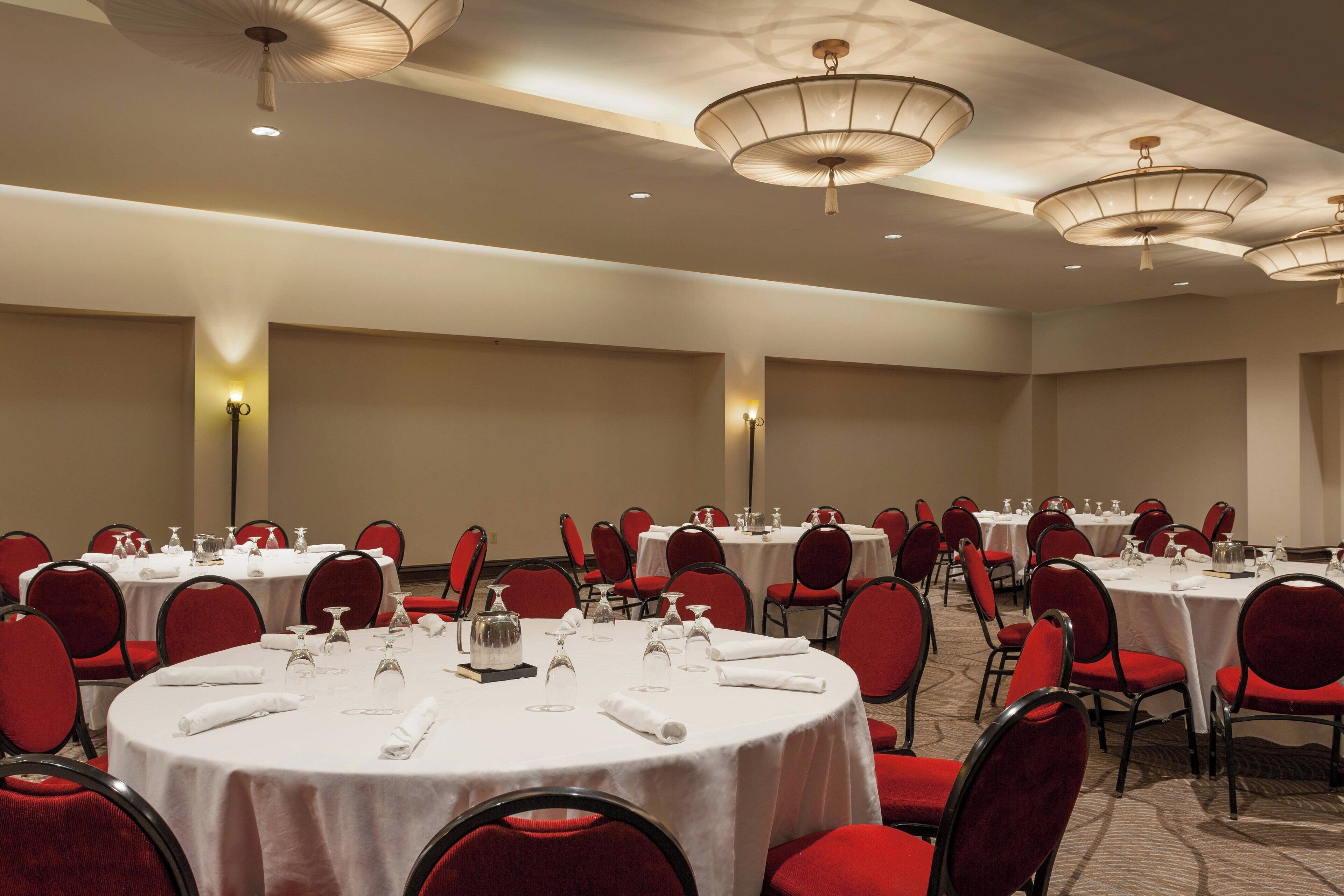 A banquet hall with round tables, red chairs, and white tablecloths.