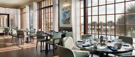 A spacious dining area with large windows, multiple tables, and chairs.
