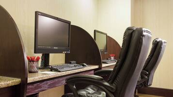 A hotel workspace with two computer monitors, a keyboard, and a leather chair.
