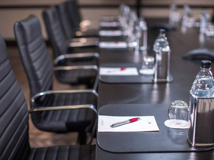 A conference room with black leather chairs, a long table with water bottles, glasses, and a pen.