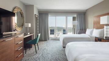A hotel room with two beds, a desk, a chair, a TV, and a balcony with a view.