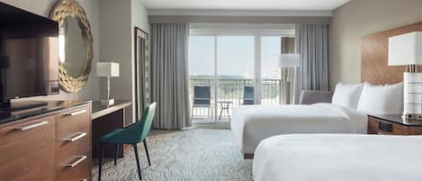 A hotel room with two beds, a desk, a chair, a TV, and a balcony with a view.