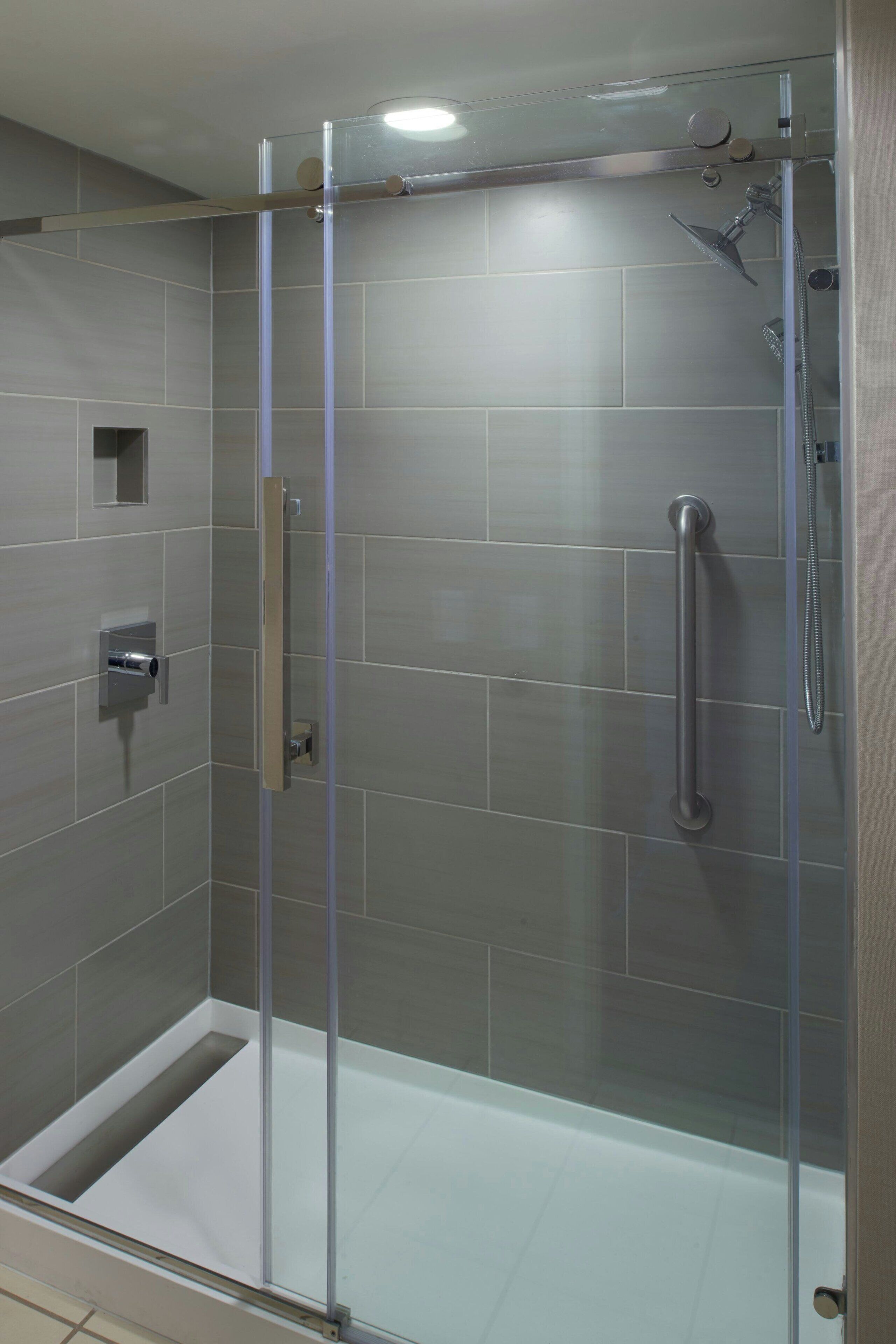 Una ducha moderna con puerta de cristal, cabezal de ducha de mano y control de ducha manual.