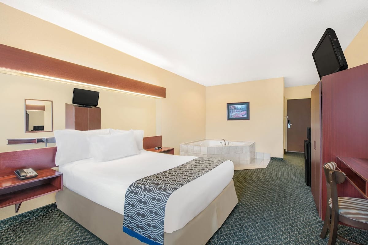 A hotel room with a bed, a desk with a telephone, a television, a bathroom with a bathtub, and a wardrobe.