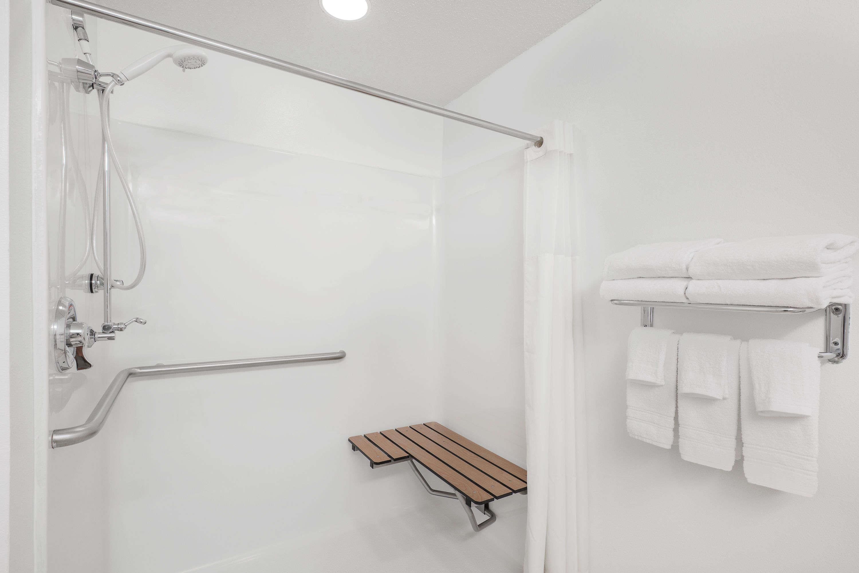 Un baño moderno con ducha acristalada, un banco de madera y un perchero con toallas dobladas.