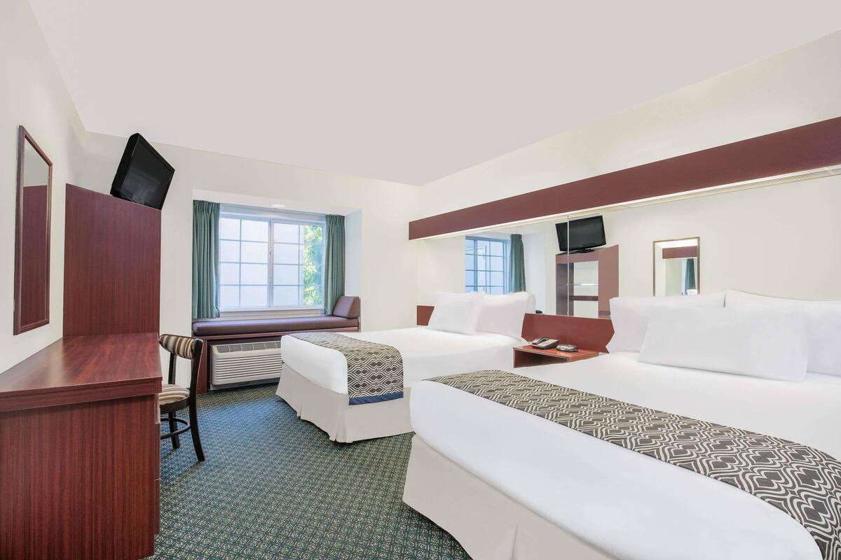 A hotel room with two beds, a desk, a chair, a TV, and a window with curtains.