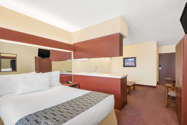 Una habitación de hotel con una cama grande, un escritorio con lavabo, un televisor y un espejo.