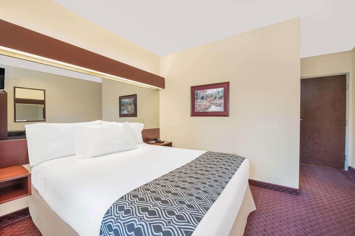 A hotel room with a bed, a nightstand, a mirror, and two framed pictures on the wall.