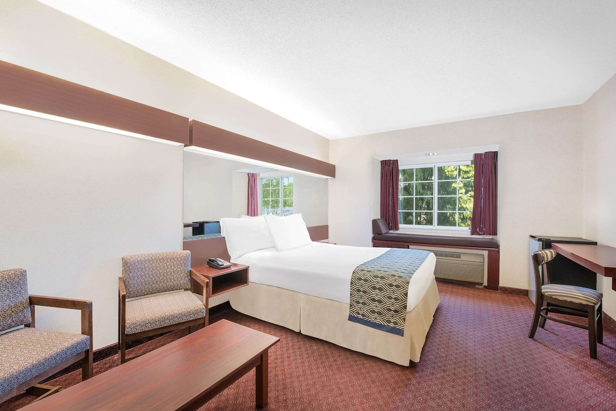 A hotel room with a bed, two armchairs, a desk, and a window with curtains.