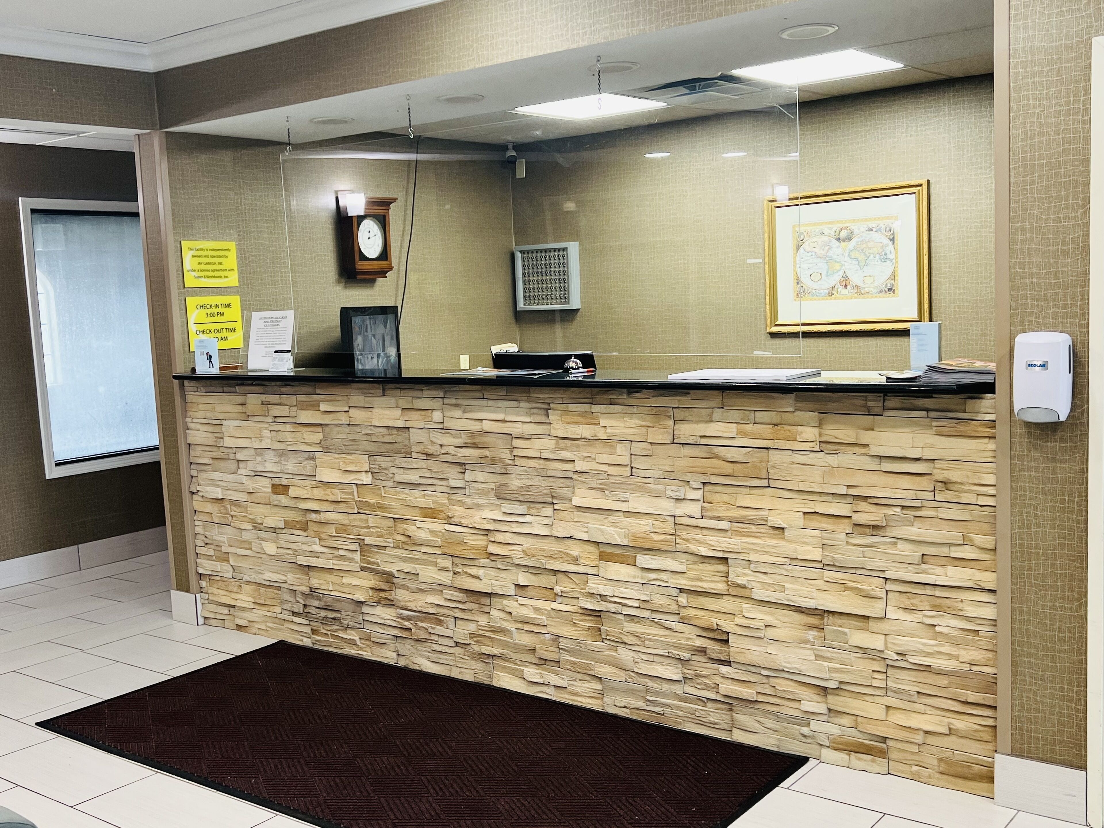 Un área de recepción con pared de piedra, un reloj, un mapa enmarcado y un cartel con los horarios de registro de entrada y salida.