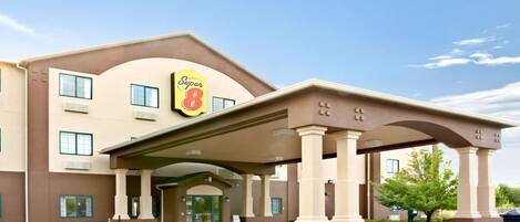 A Super 8 hotel with a covered entrance, multiple windows, and a landscaped area with a bench and small trees.