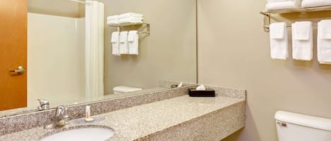 Un baño con encimera de granito, dos lavamanos, inodoro, toallero y espejo.