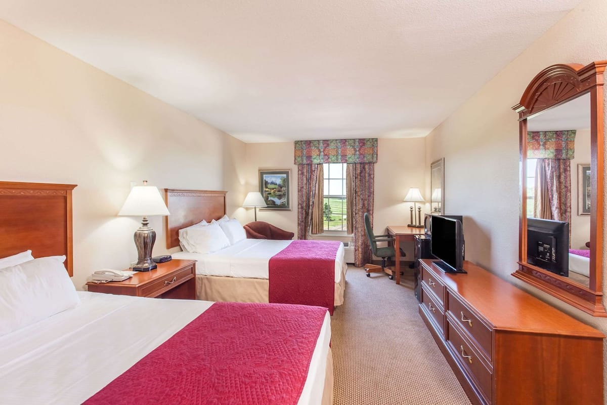 A hotel room with two beds, a desk, a television, and a mirror.
