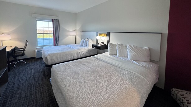 A hotel room with two beds, a desk, a chair, and a window with curtains.