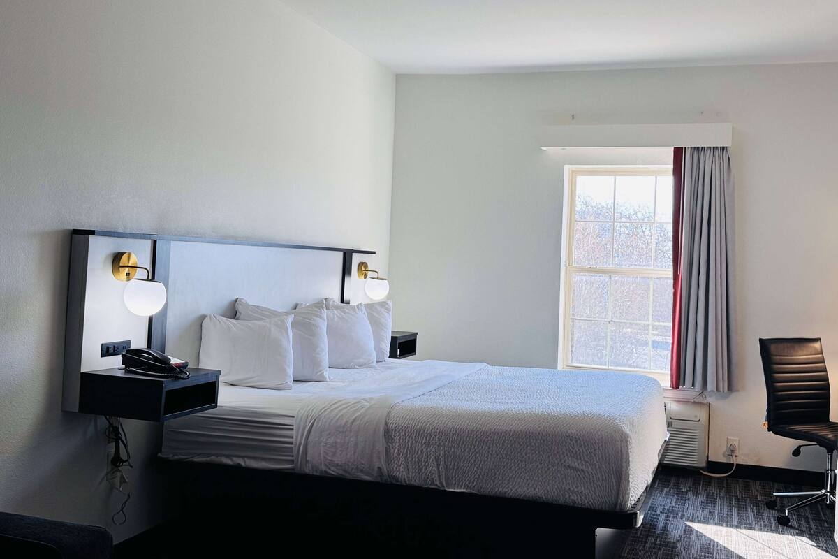 A hotel room with a large bed, bedside lamps, a desk, and a chair.