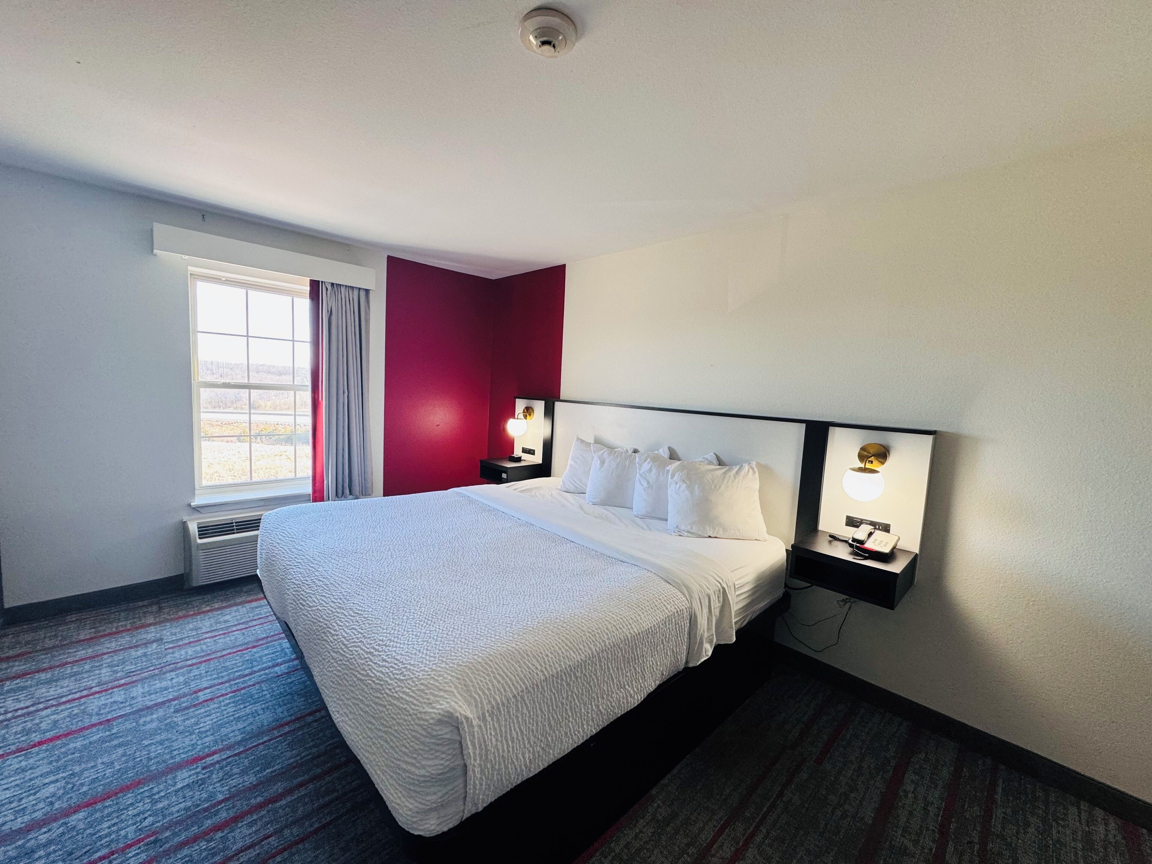 Een hotelkamer met een groot bed, een raam met gordijnen, een wandlampje op een nachtkastje en een radiator.