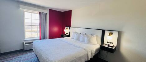 Een hotelkamer met een groot bed, een raam met gordijnen, een wandlampje op een nachtkastje en een radiator.