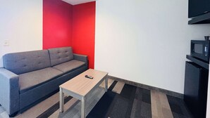 A modern living room with a grey sofa, a small wooden table, and a red accent wall.
