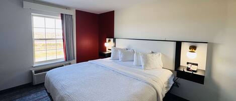 A hotel room with a large bed, two bedside tables with lamps, a window with curtains, and a red accent wall.