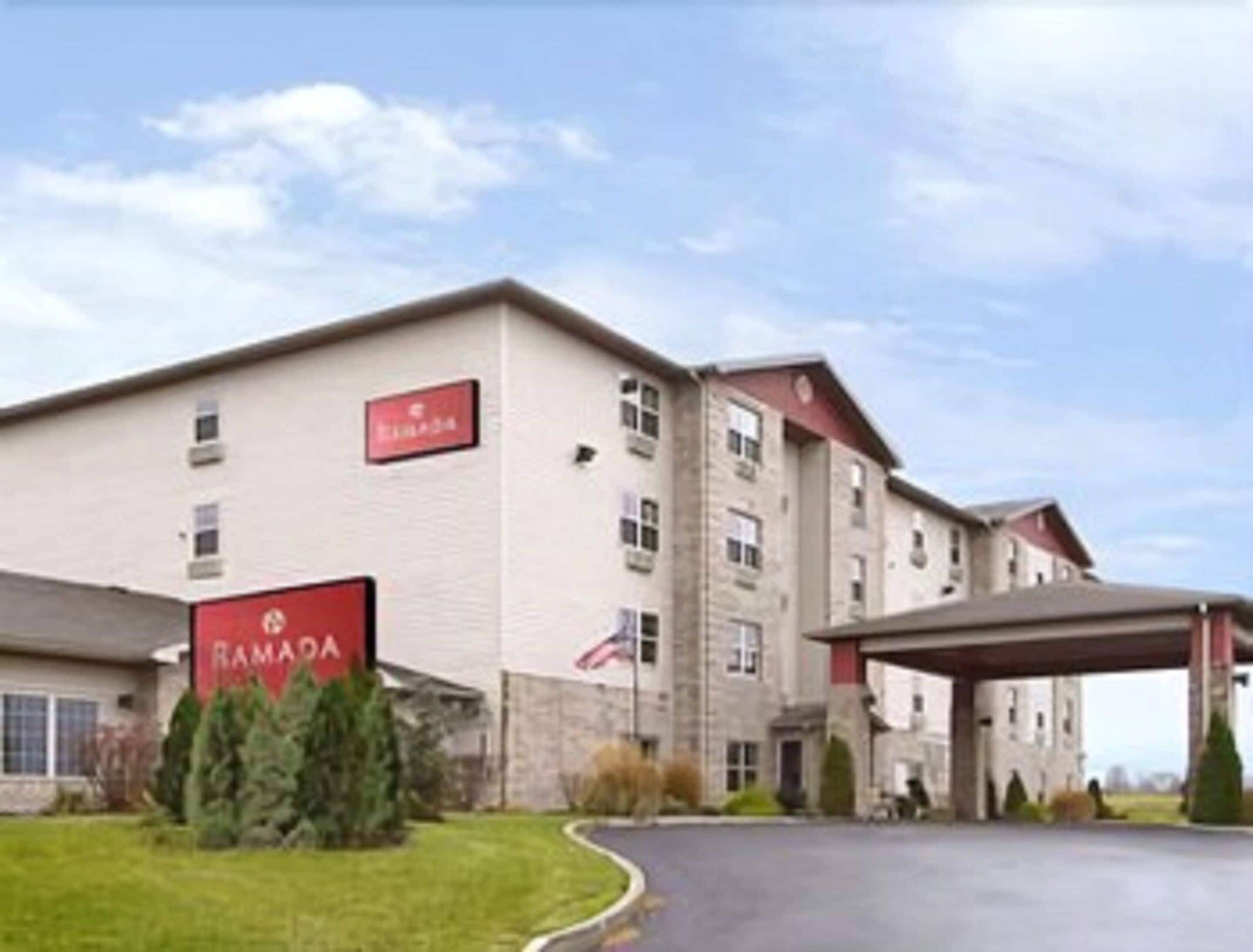 A Ramada hotel with a large building, a covered parking area, and a well-maintained lawn.