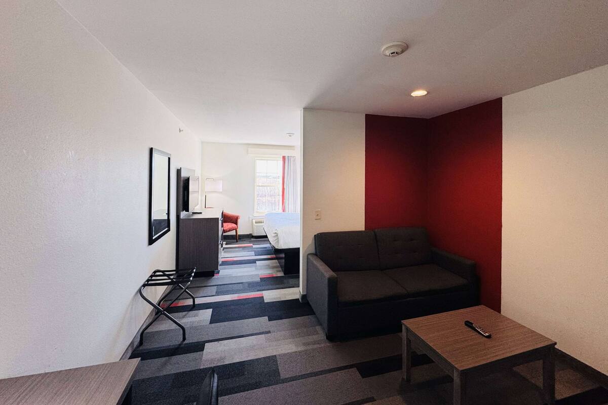A modern hotel room with a sofa, a small table, a TV, and a red accent wall.