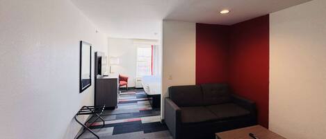 Una habitación de hotel moderna con sofá, una mesita, televisión y una pared decorada en rojo.