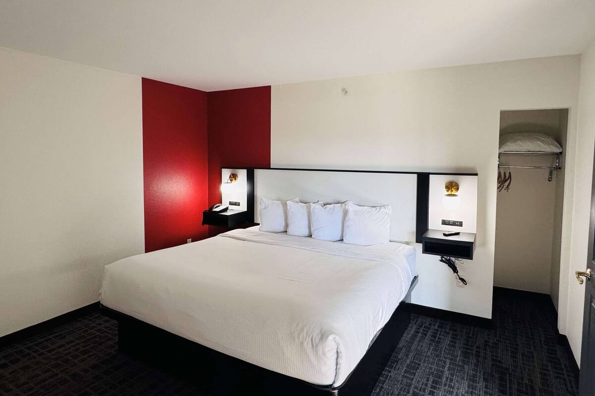 A hotel room with a large bed, two bedside tables with lamps, a red accent wall, and a door leading to a bathroom.
