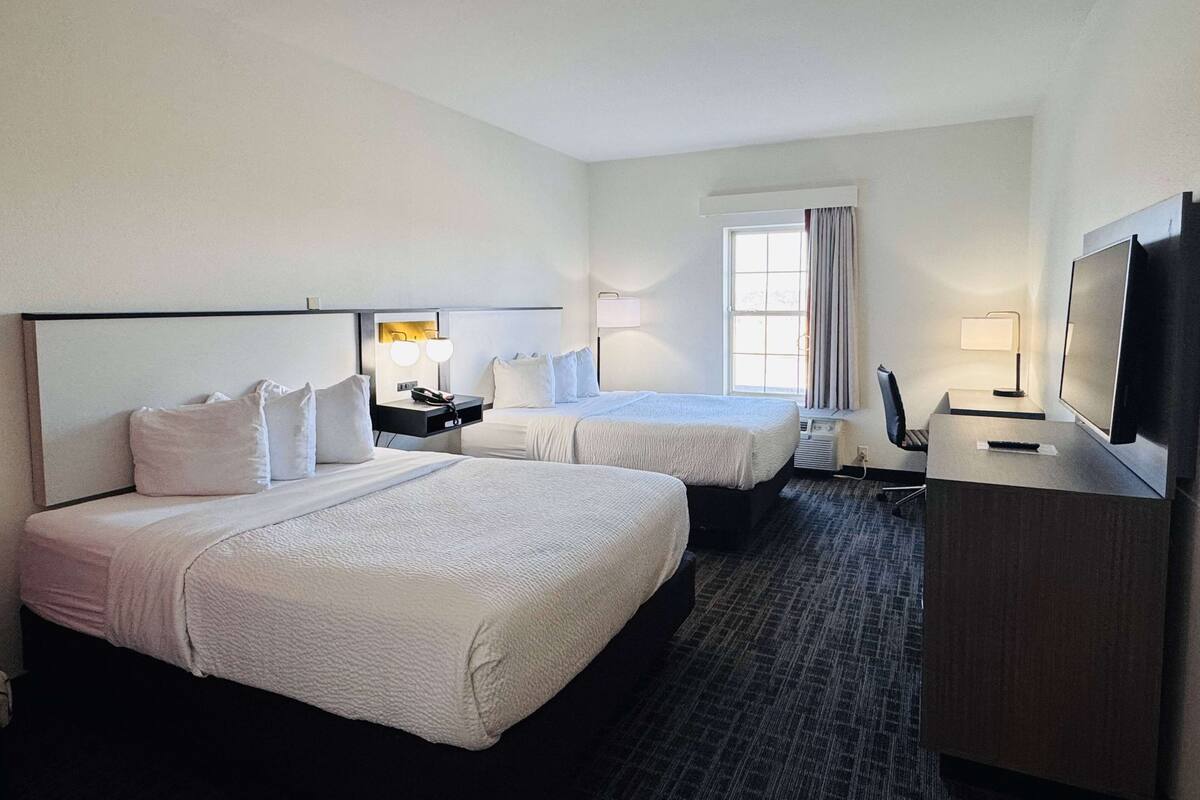 A hotel room with two beds, a desk, a TV, and a window with curtains.