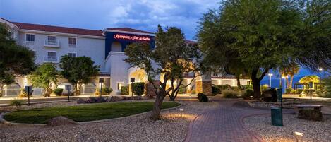 Un hotel con un camino empedrado, jardín ajardinado y un letrero que dice 'Hampton Inn & Suites'.