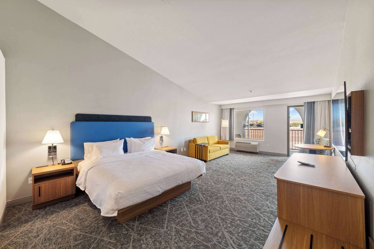 A hotel room with a large bed, a desk, a sofa, and a view of the outdoors.