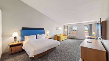 A hotel room with a large bed, a desk, a sofa, and a view of the outdoors.