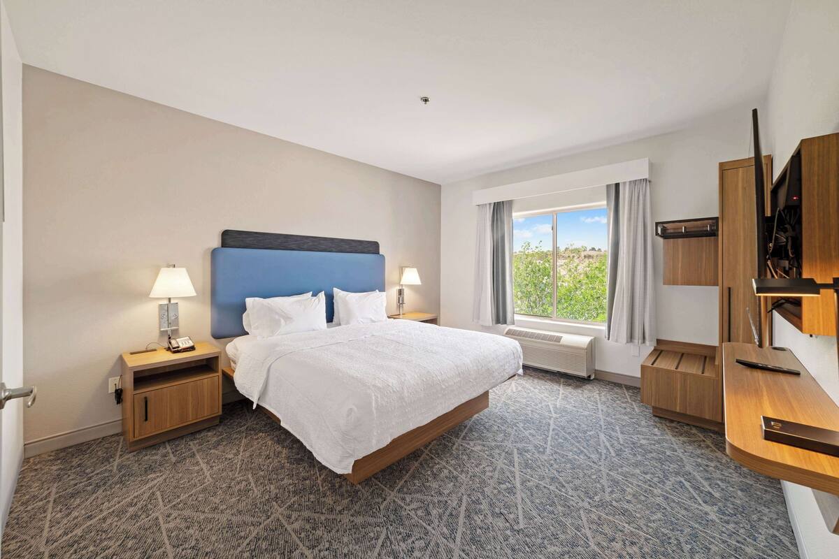 A hotel room with a large bed, two bedside tables with lamps, a TV, and a window with curtains.