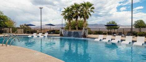 A swimming pool with lounge chairs, palm trees, and a mountain backdrop.